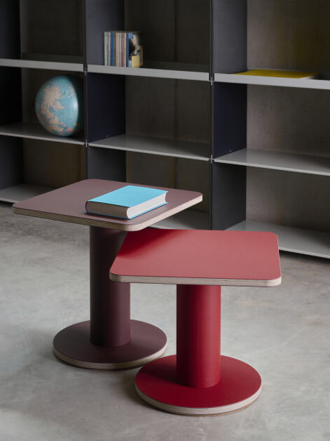 Two nesting square Off-cut side tables with plywood tabletops covered with burgundy and salsa linoleum, serving as side tables in front of a shelf.