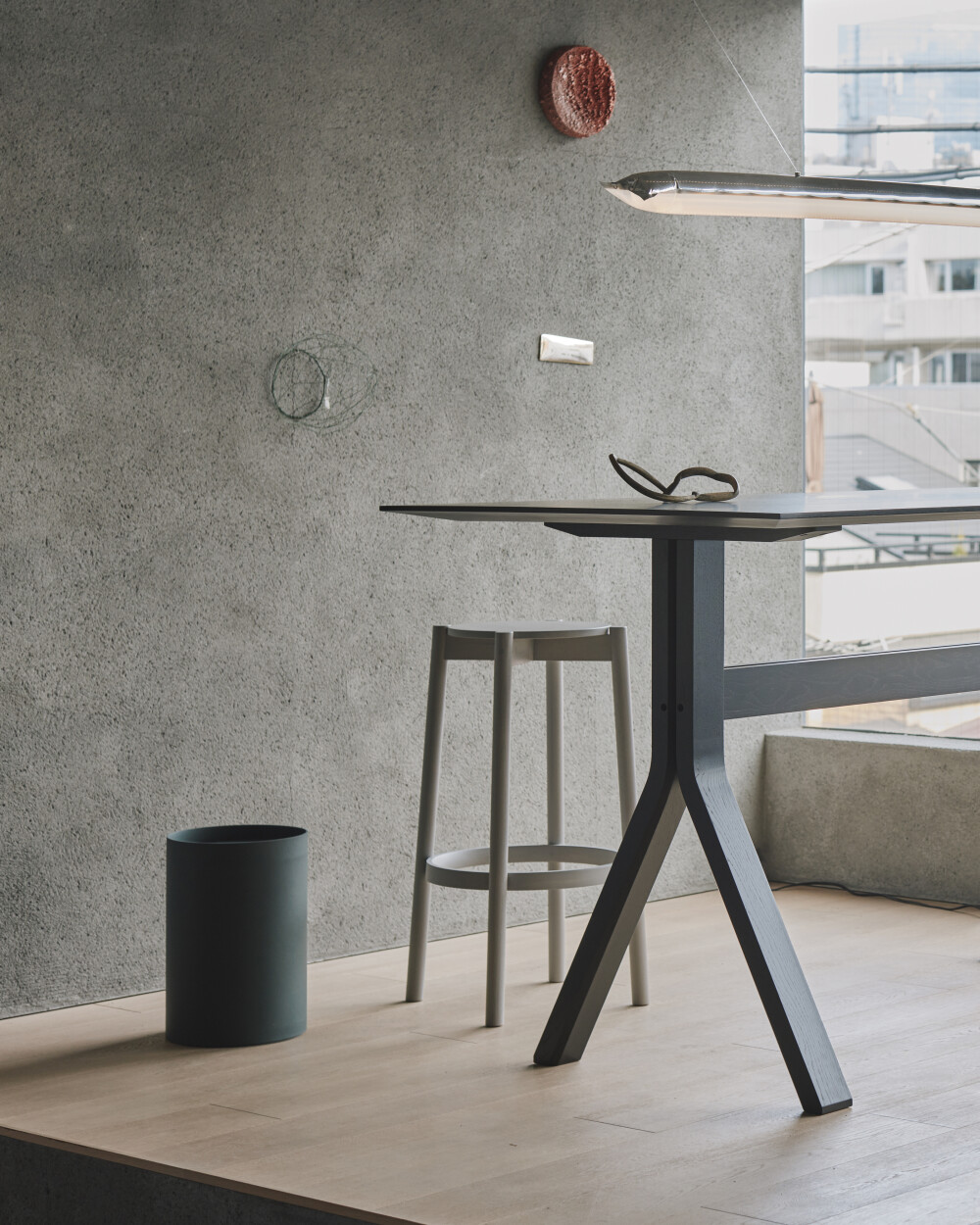 TIDY waste bin made of dark green linoleum, placed in a modern office with a grey concrete wall, high table and two stools.