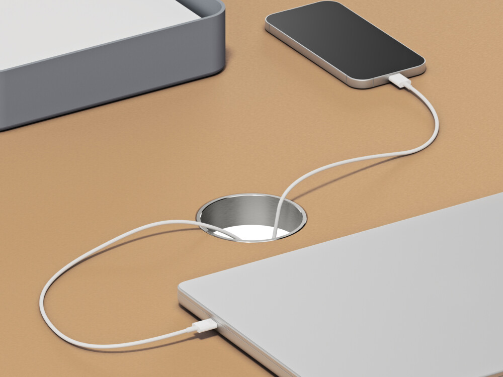 Aluminium-Kabeldurchlass, rund und eingelassen in Linoleum-Tischplatte von Faust – mit sichtbaren Ladekabeln für Laptop und Smartphone.