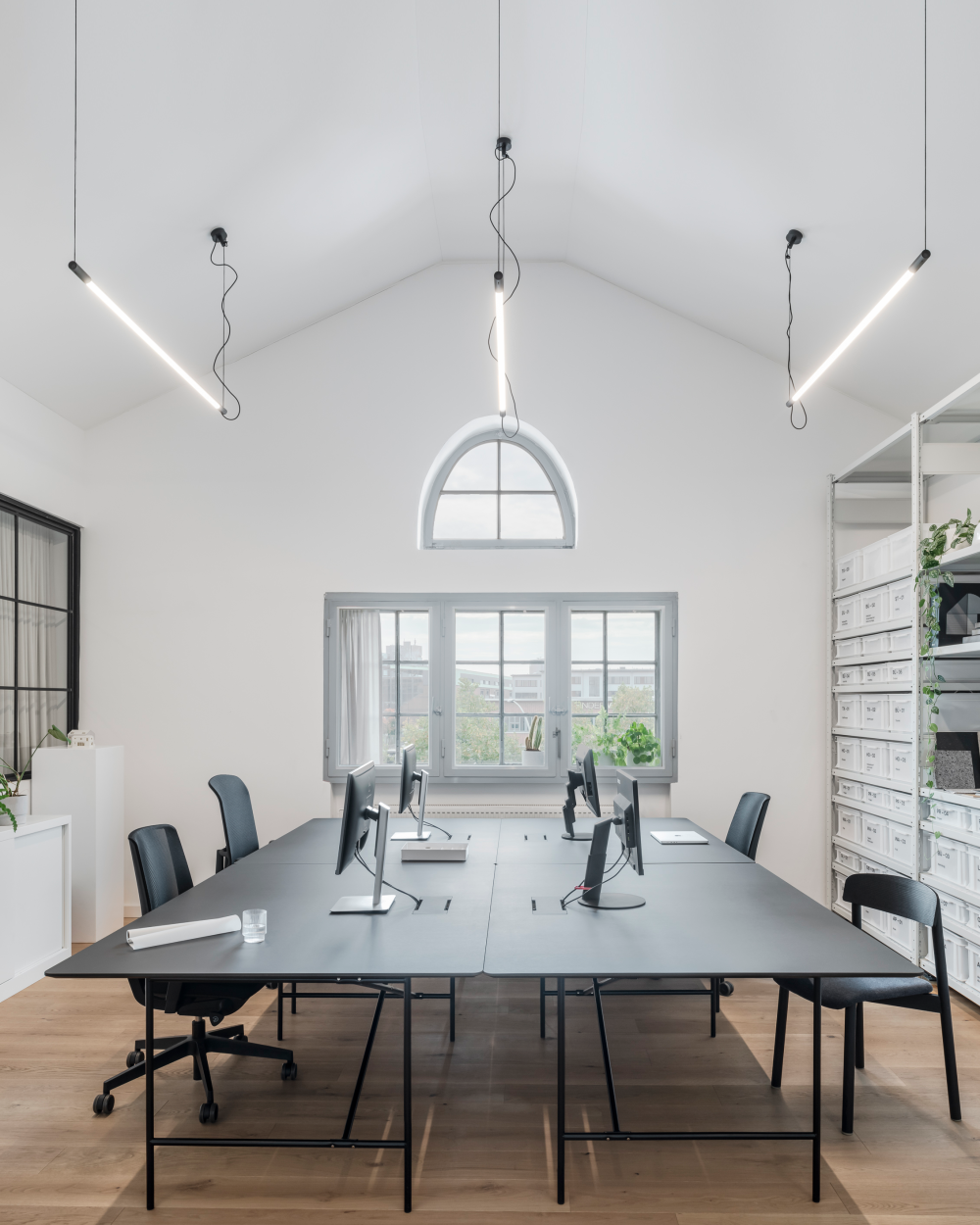 E2 desks with black linoleum tops in a bright office, used as large workbenches with monitors.