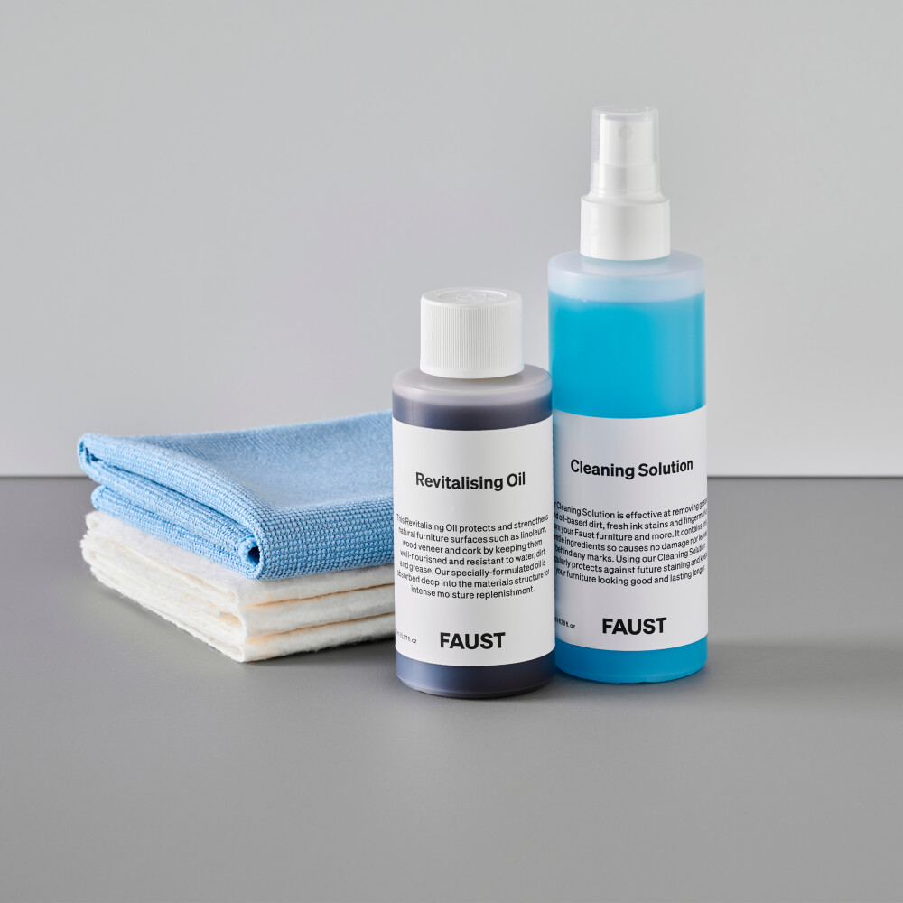 A set of Faust care products containing a revitalising oil and cleaning solution in semi-transparent bottles with branded labels. In the background, three white cotton cloths and one light blue microfibre towel.