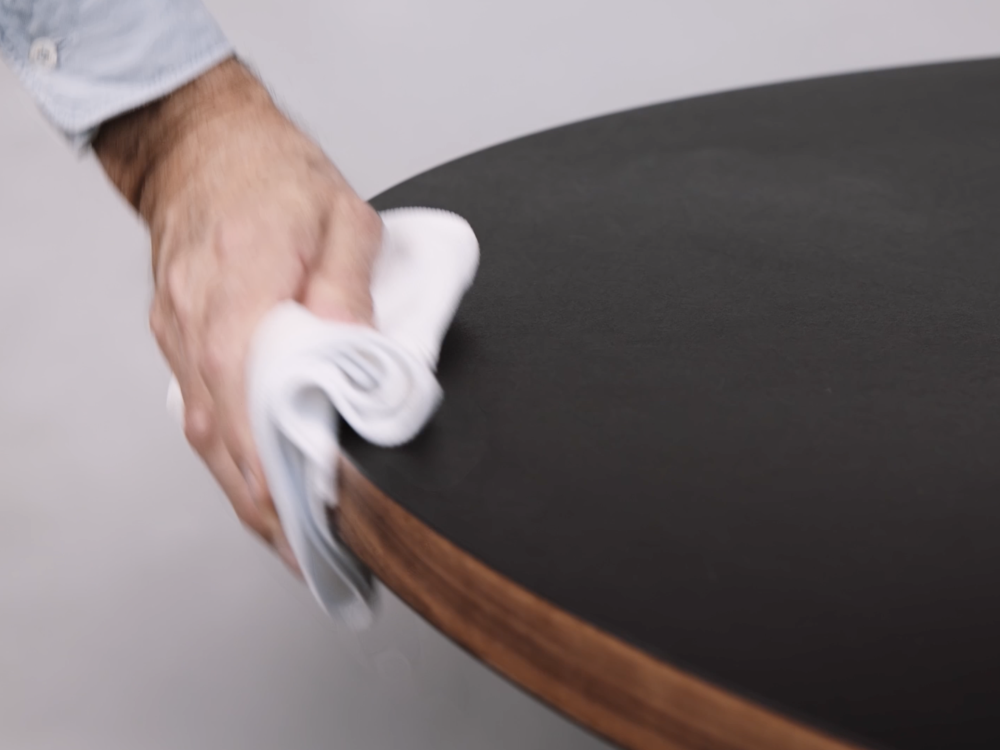 Person reinigt eine Linoleum-Tischplatte mit einer Reinigungslösung und Pflegeöl.