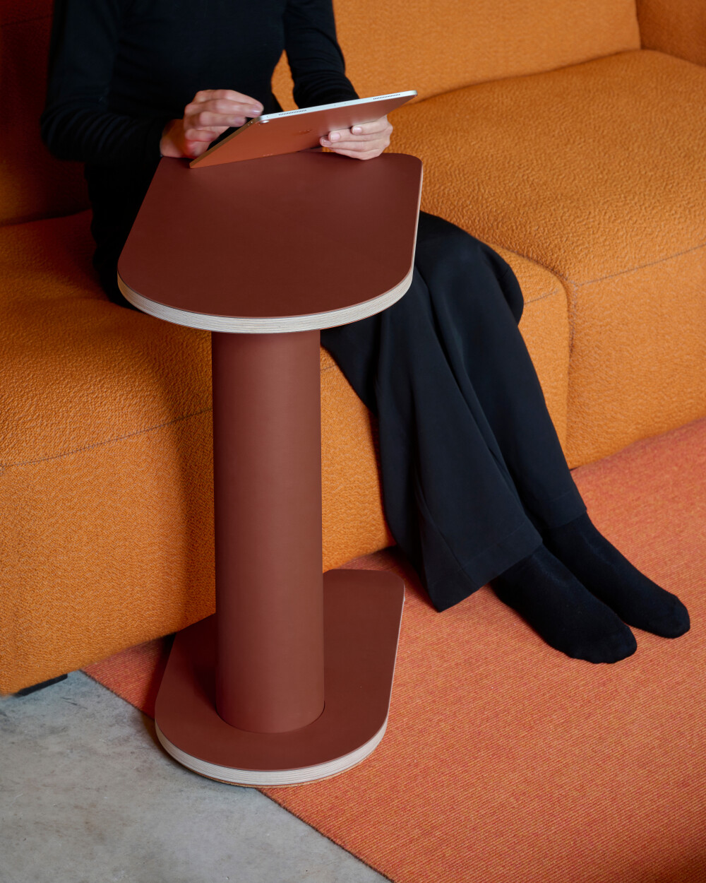OFF-CUT side table by Faust with roter linoleum surface, used as a shelf for a tablet next to an orange sofa.