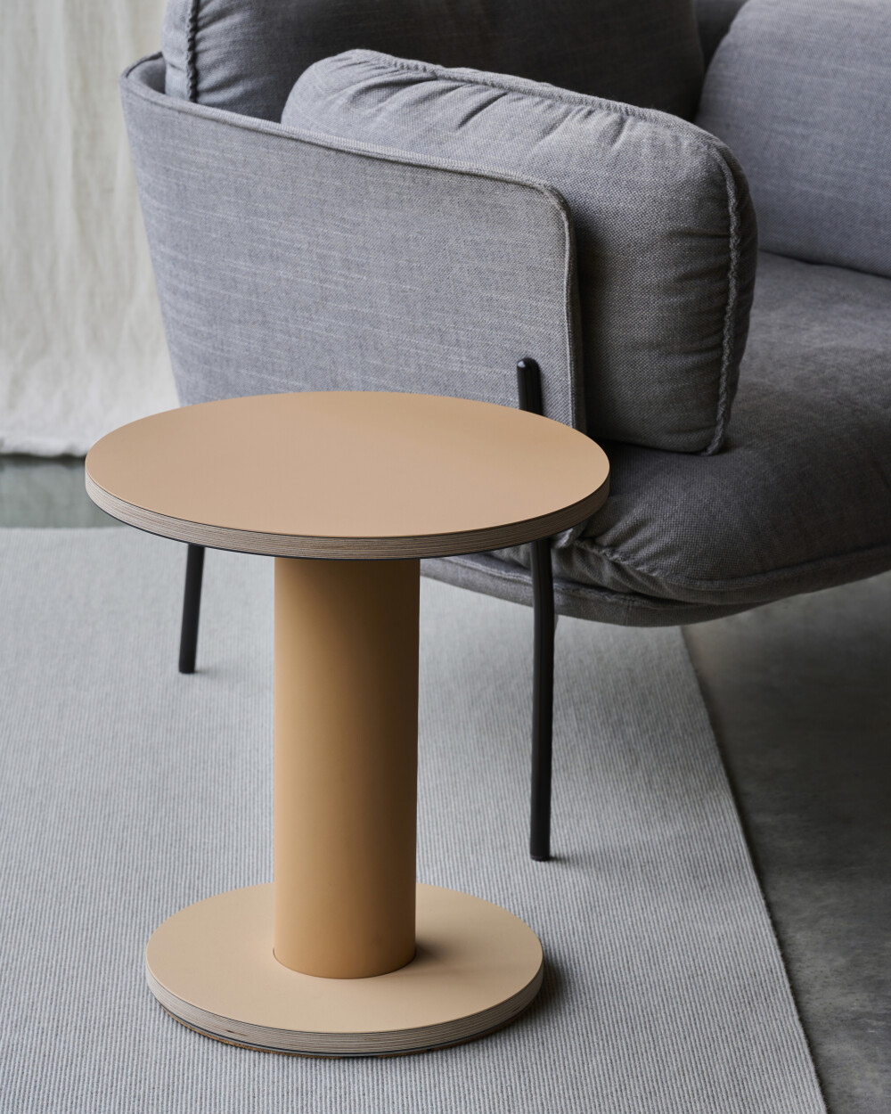 Round OFF-CUT side table with linoleum-coated surface, placed next to a gray sofa in a modern living room
