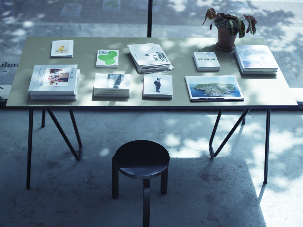 Table with dark Sinus trestles in deep black and a olive-coloured top, arranged with books and a plant.