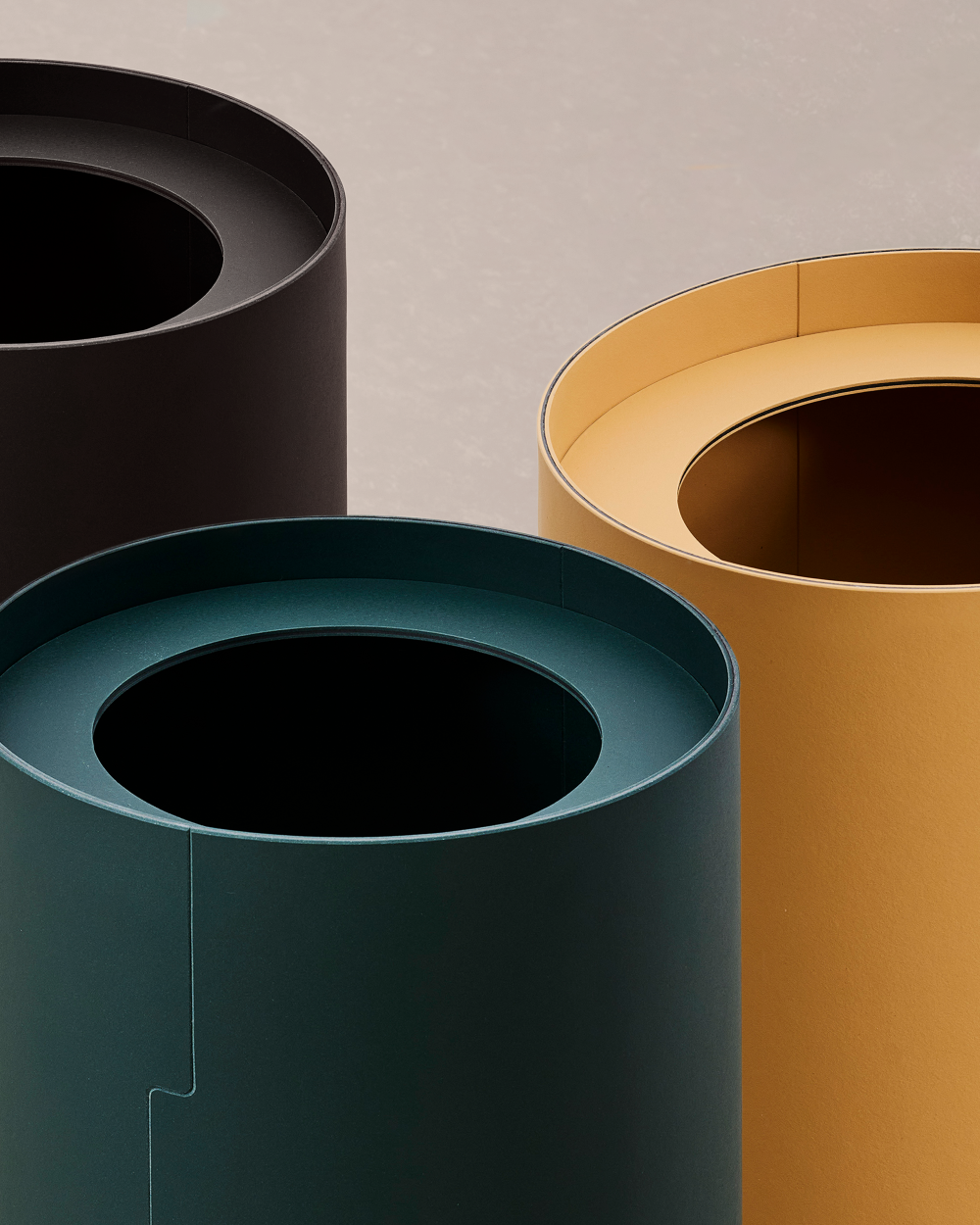 Three TIDY wastepaper baskets in black, dark green and ochre with round openings, photographed from above.