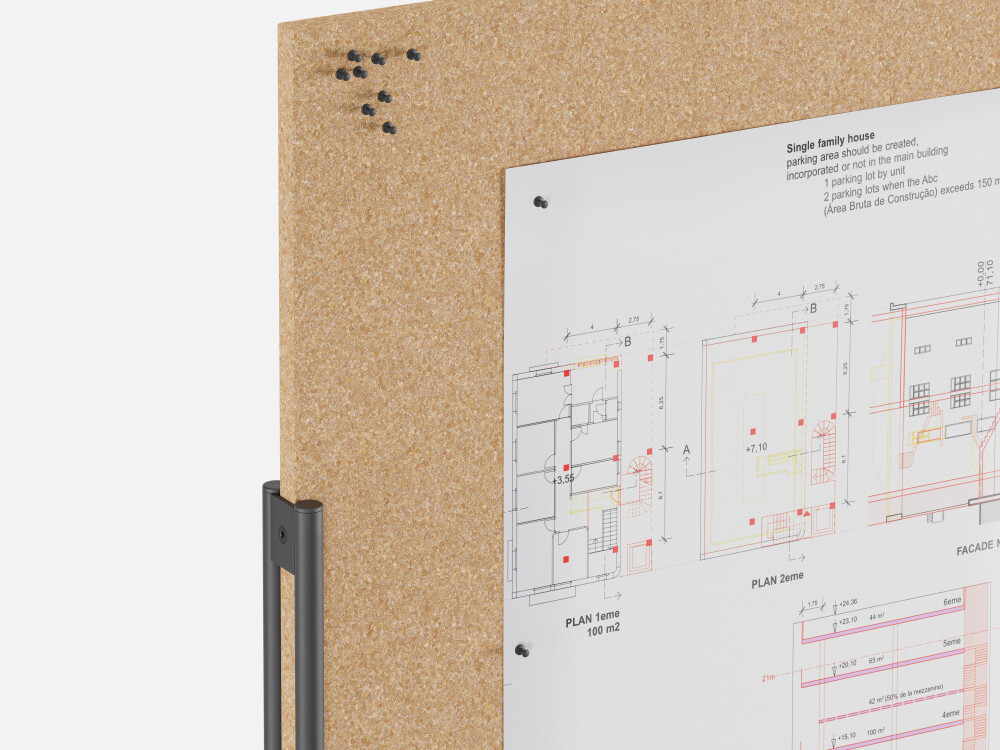Detailed view of the WALL pinboard with cork surface, equipped with black pins and an attached architectural plan.