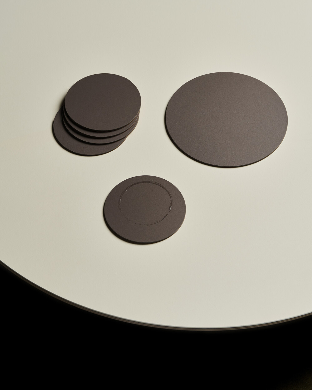 PAD Untersetzer aus Linoleum in Mauve auf heller Tischoberfläche, mit gestapelten und einzeln Untersetzern in verschiedenen Größen.