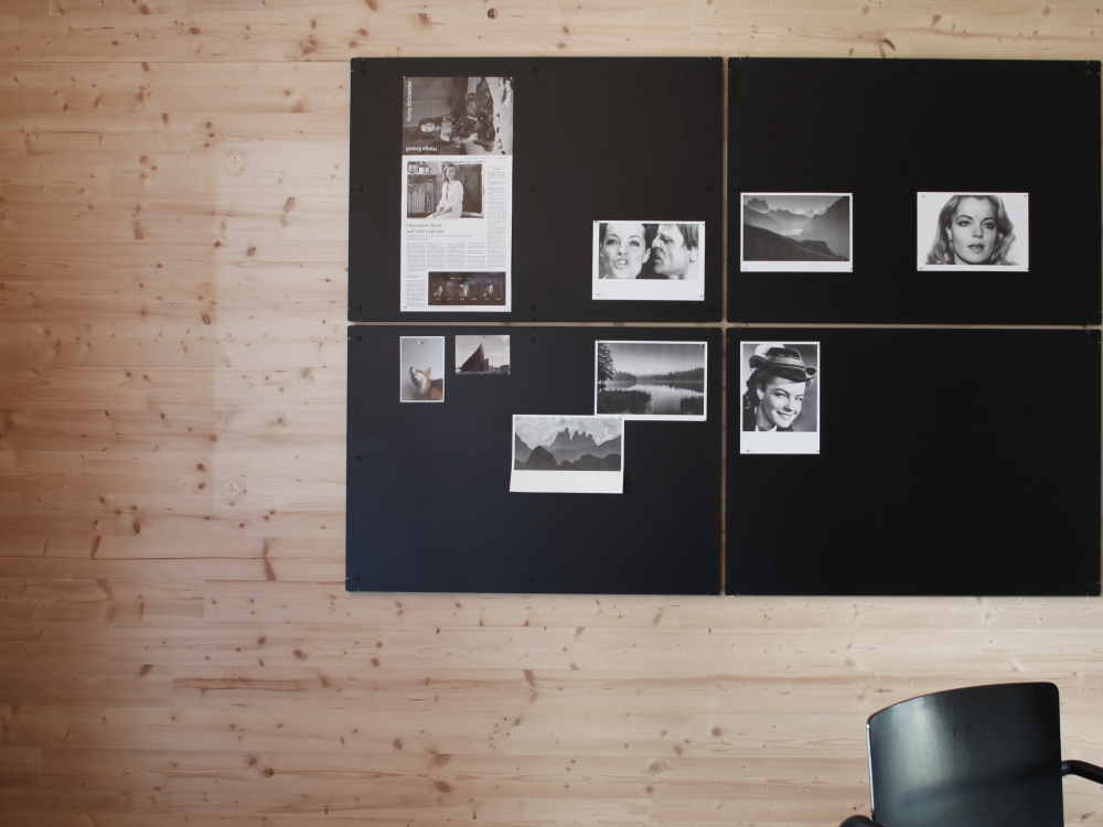 Four black PIN magnetic boards made of steel on a wooden wall with photographs pinned to them.