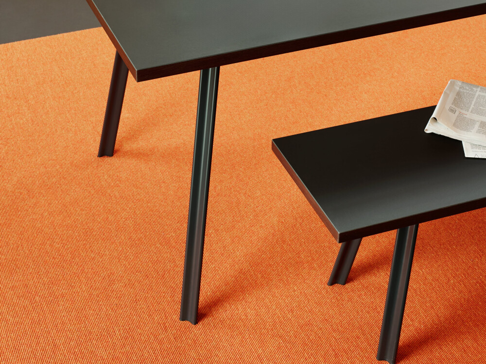 Detailed view of BEAM bench and table with black linoleum on orange carpet, with white crockery and espresso pot.