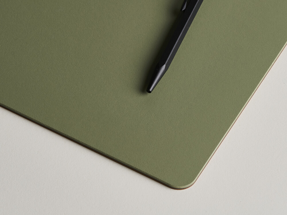Close-up of a PAD writing pad made of olive-coloured linoleum with rounded corners and a black pen on it.