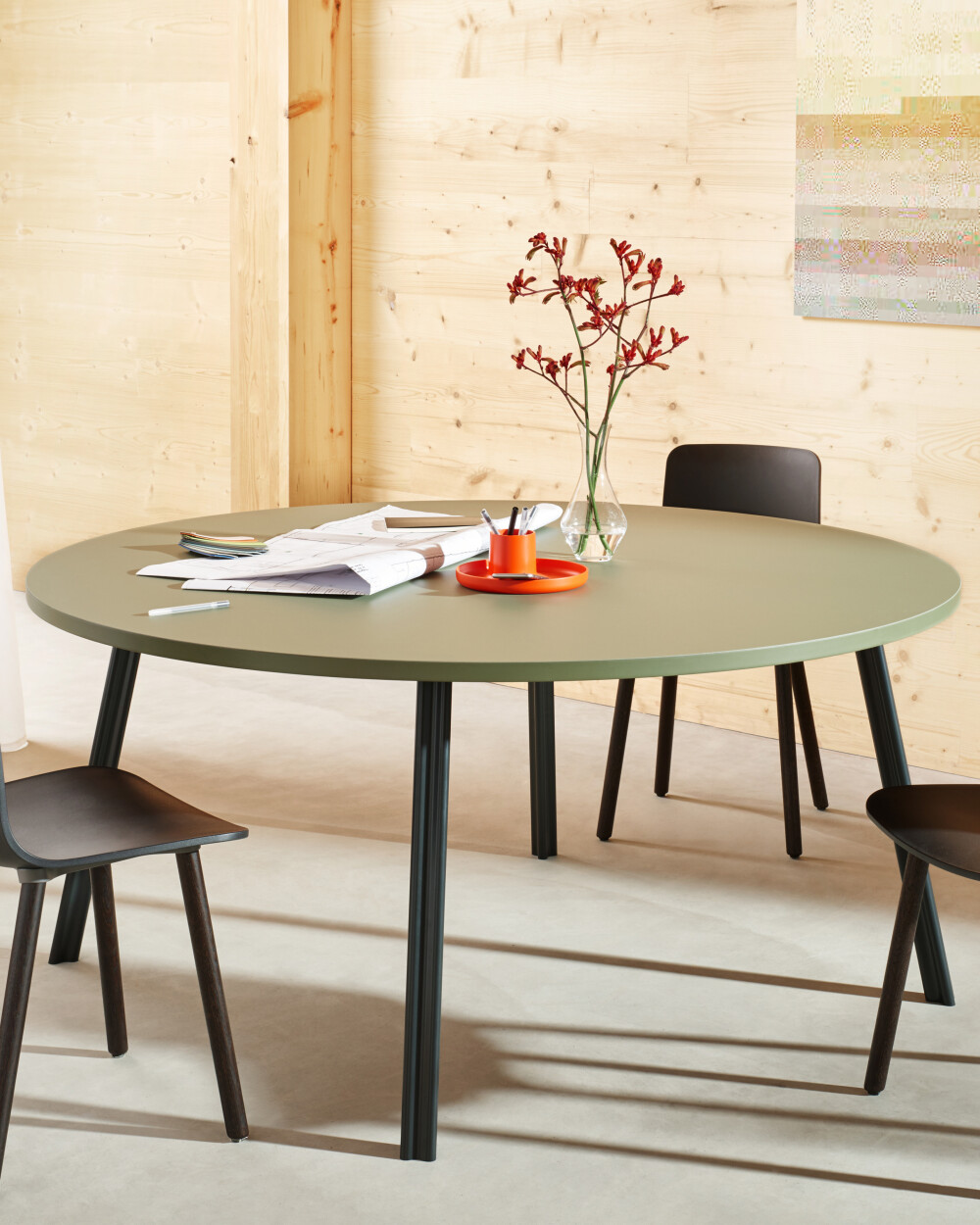Round BEAM table with olive-colored top in a modern room, used as a meeting table with chairs and work documents.